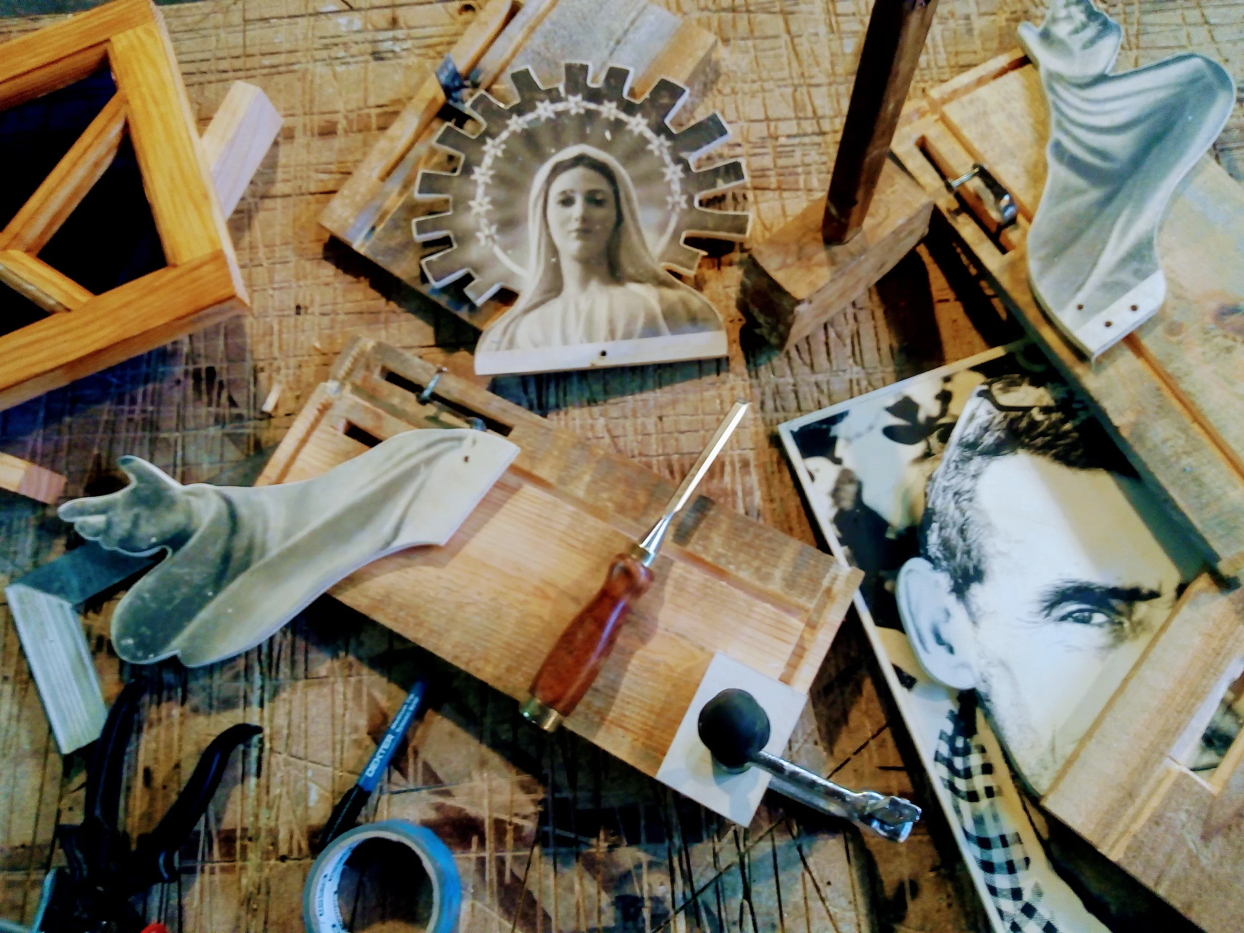 Un établi de bois : une Vierge et des mains découpées, des outils, une photo ancienne