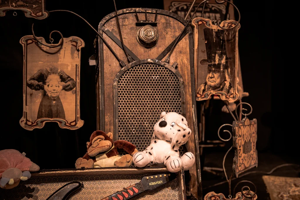 Une vieille radio en bois entre des cadres forains, deux peluches posées devant
